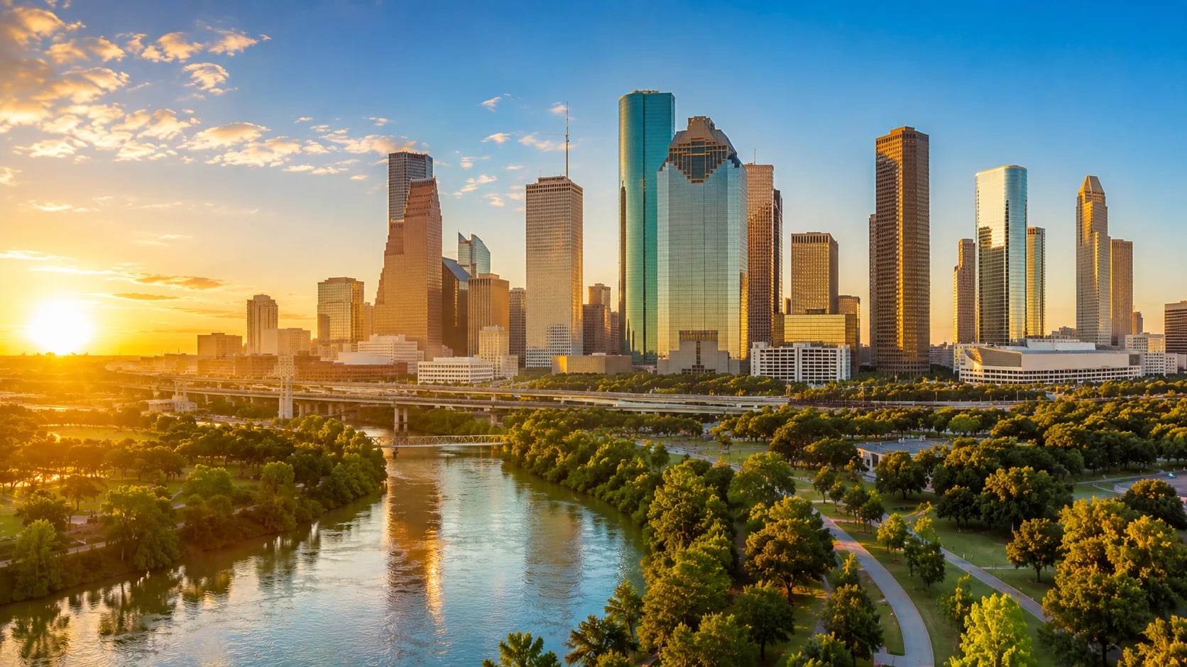 Houston skyline at sunset over Buffalo Bayou with downtown towers and green parkland