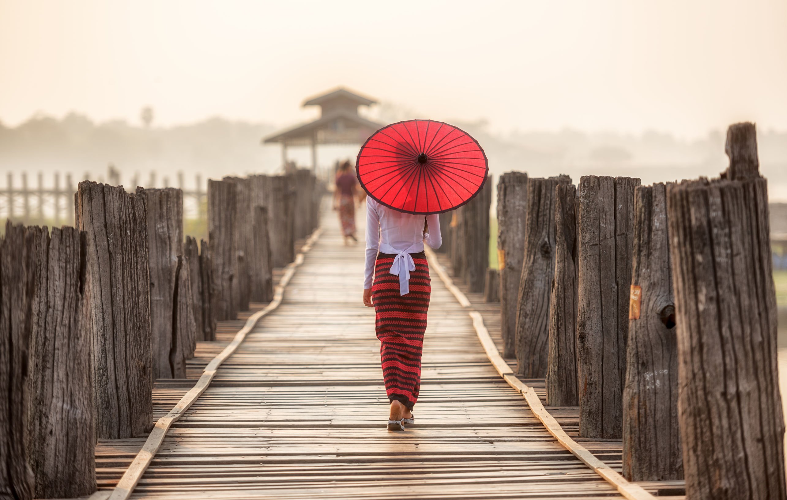 body language of an asian lady holding a red umbrella while crossing a wooden bridge shows confidence