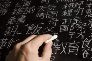 Close up of male hand writing Chinese and Japanese characters on blackboard