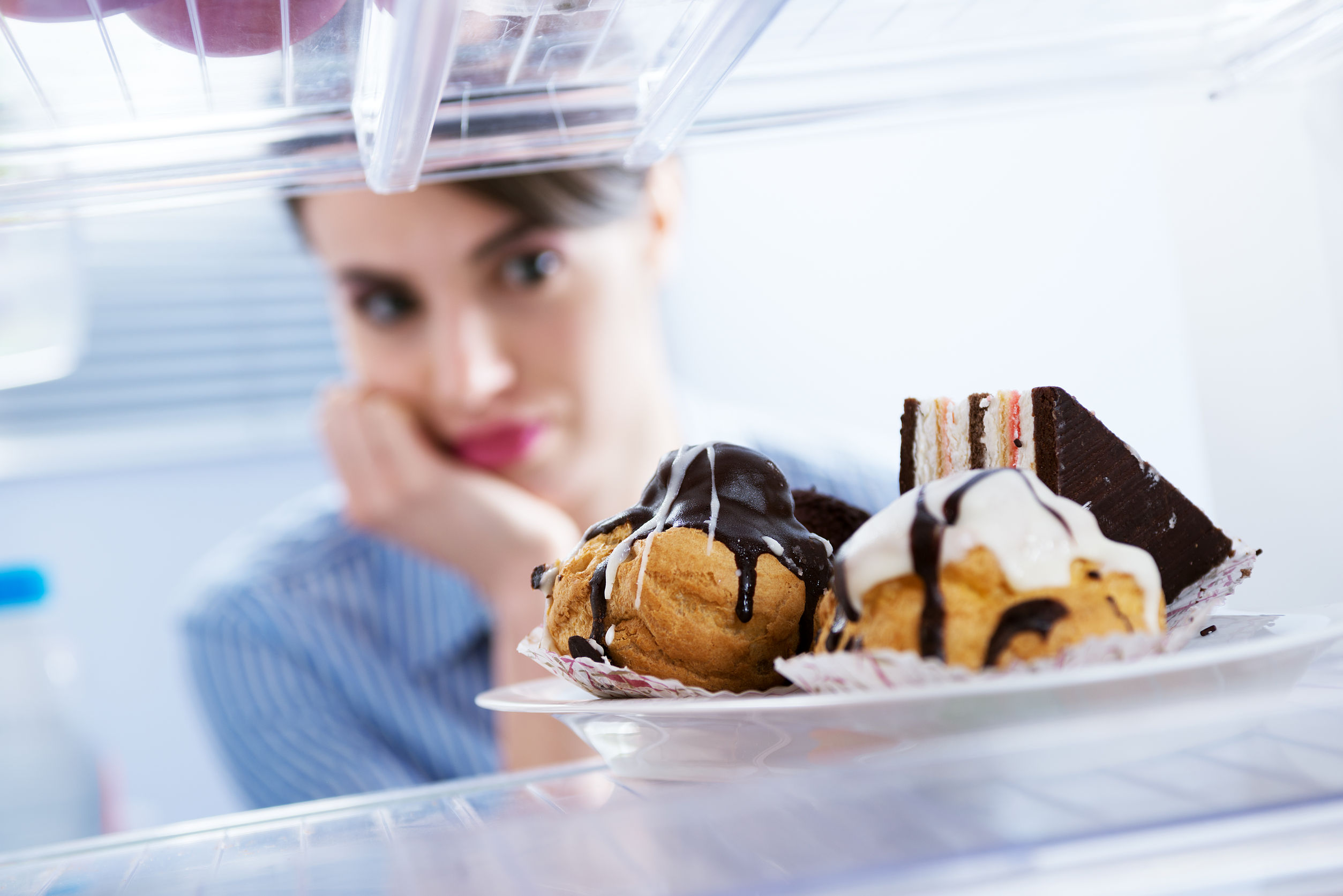 Young hungry woman in front of refrigerator craving chocolate pastries