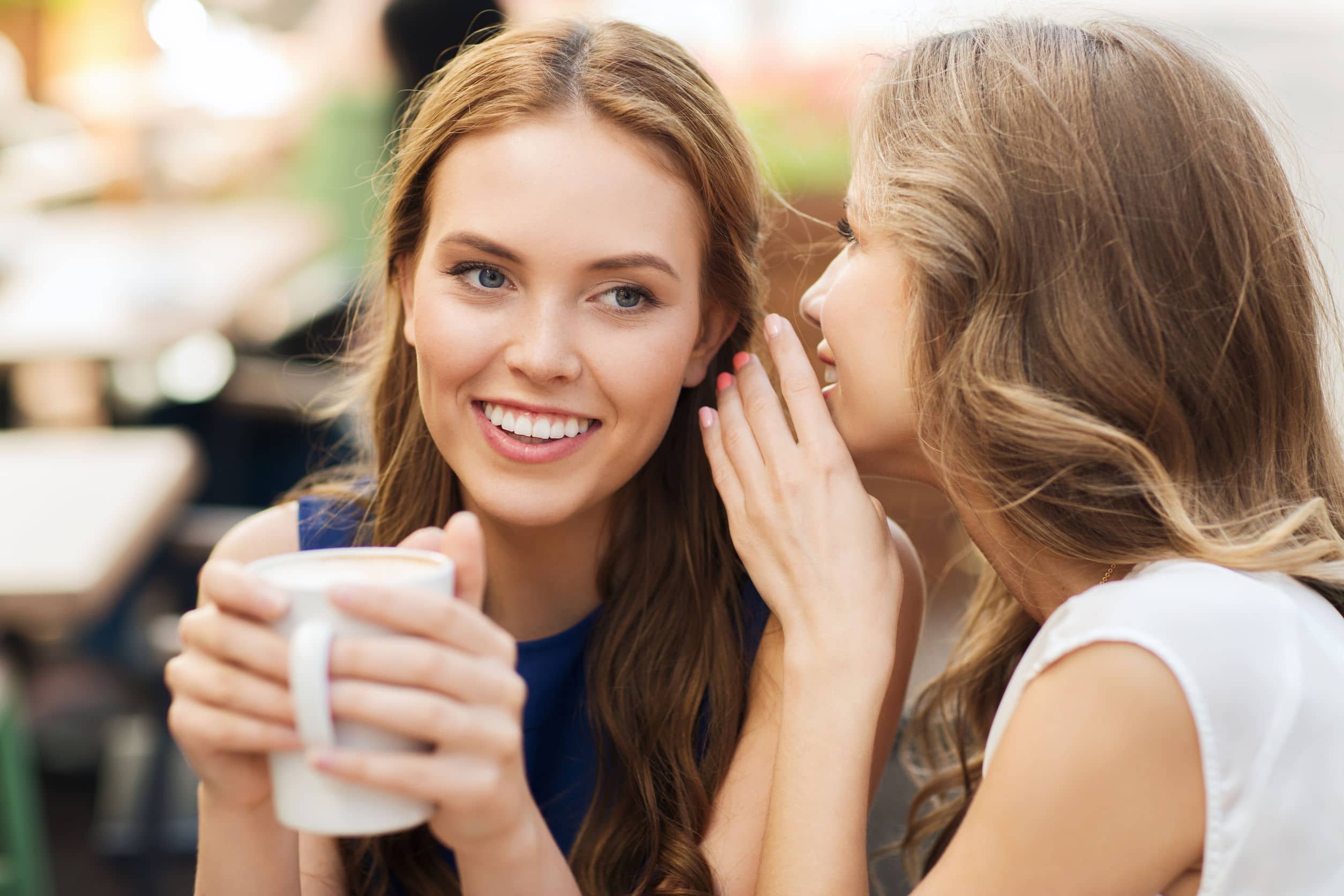smiling young women drinking coffee and talking at outdoor cafe