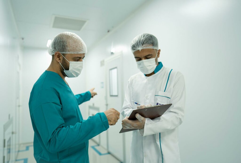 Two medical professionals in scrubs with masks and hair nets looking at a chart, translating a document.